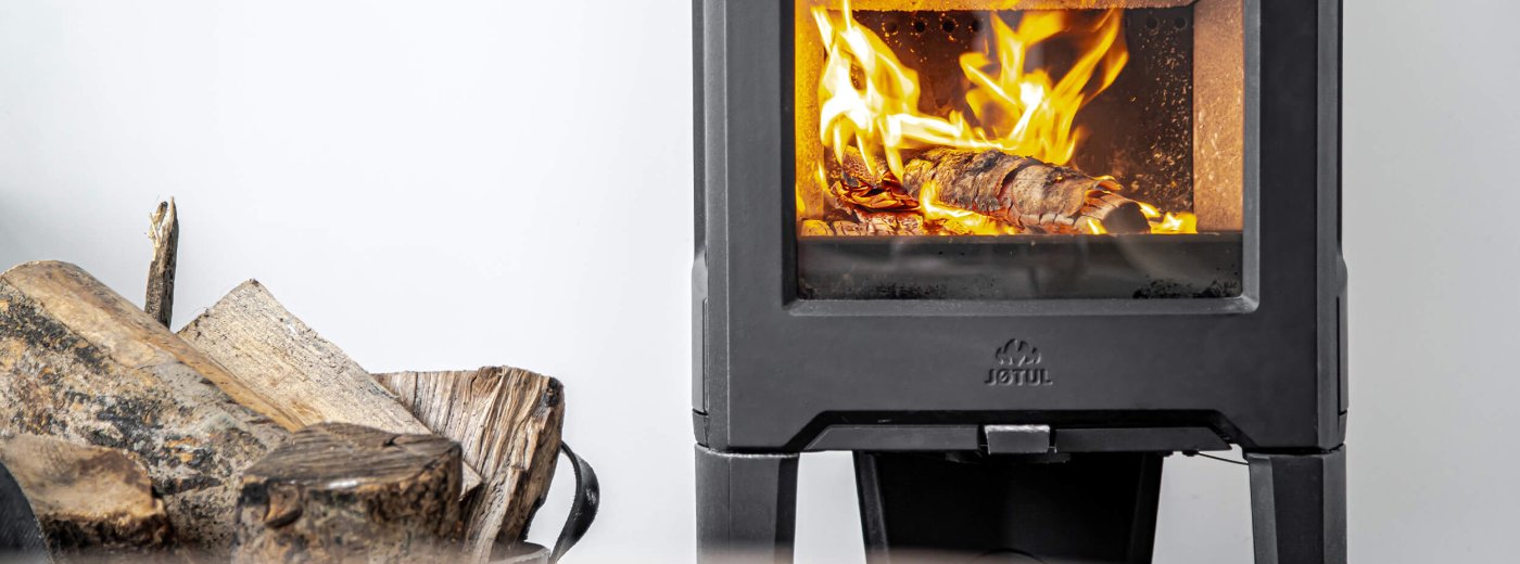 Jøtul F 163 schwarzer Holzofen mit Holzscheiten an der Seite und weißer Wand hinten 