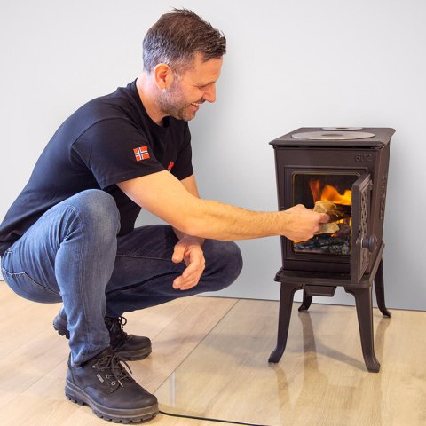 Mann legt Holz in den Kaminofen Jøtul F 602 ECO.